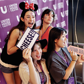 Four girls posing in front of "Union House Theatre' media wall photobooth. They all are smiling.