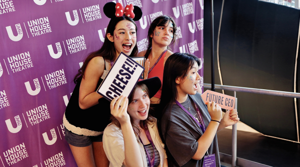 Four girls posing in front of "Union House Theatre' media wall photobooth. They all are smiling.